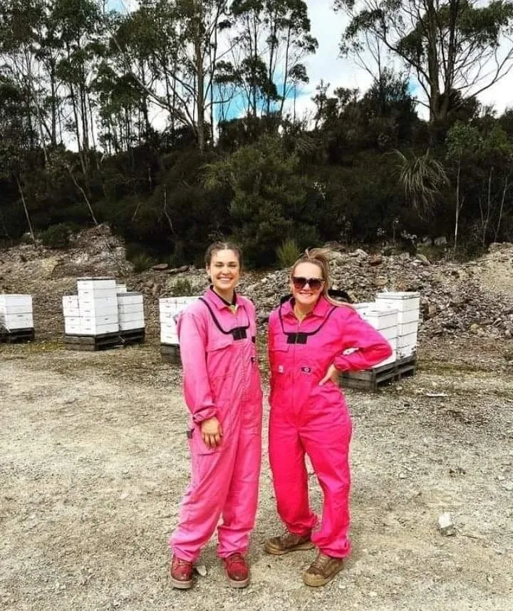 Two beekeepers in pink suits in front of white hive boxes